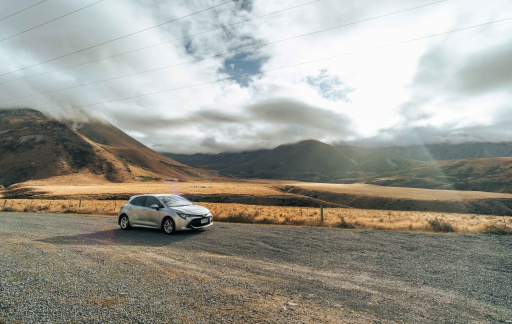 A silver car driving on the road in New Zealand with mountains in the background. What is a car loan blog