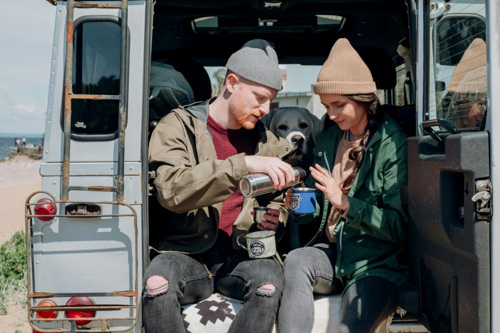 Couple sharing coffee sitting in refinanced car