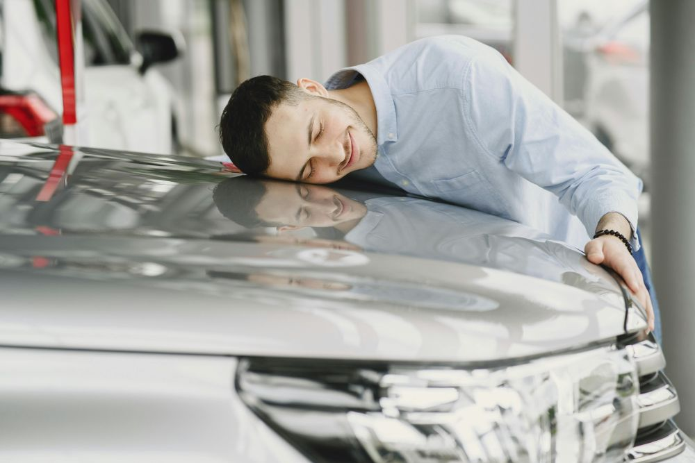 Man leaning head on bonnet of silver car asking how to refinance your car